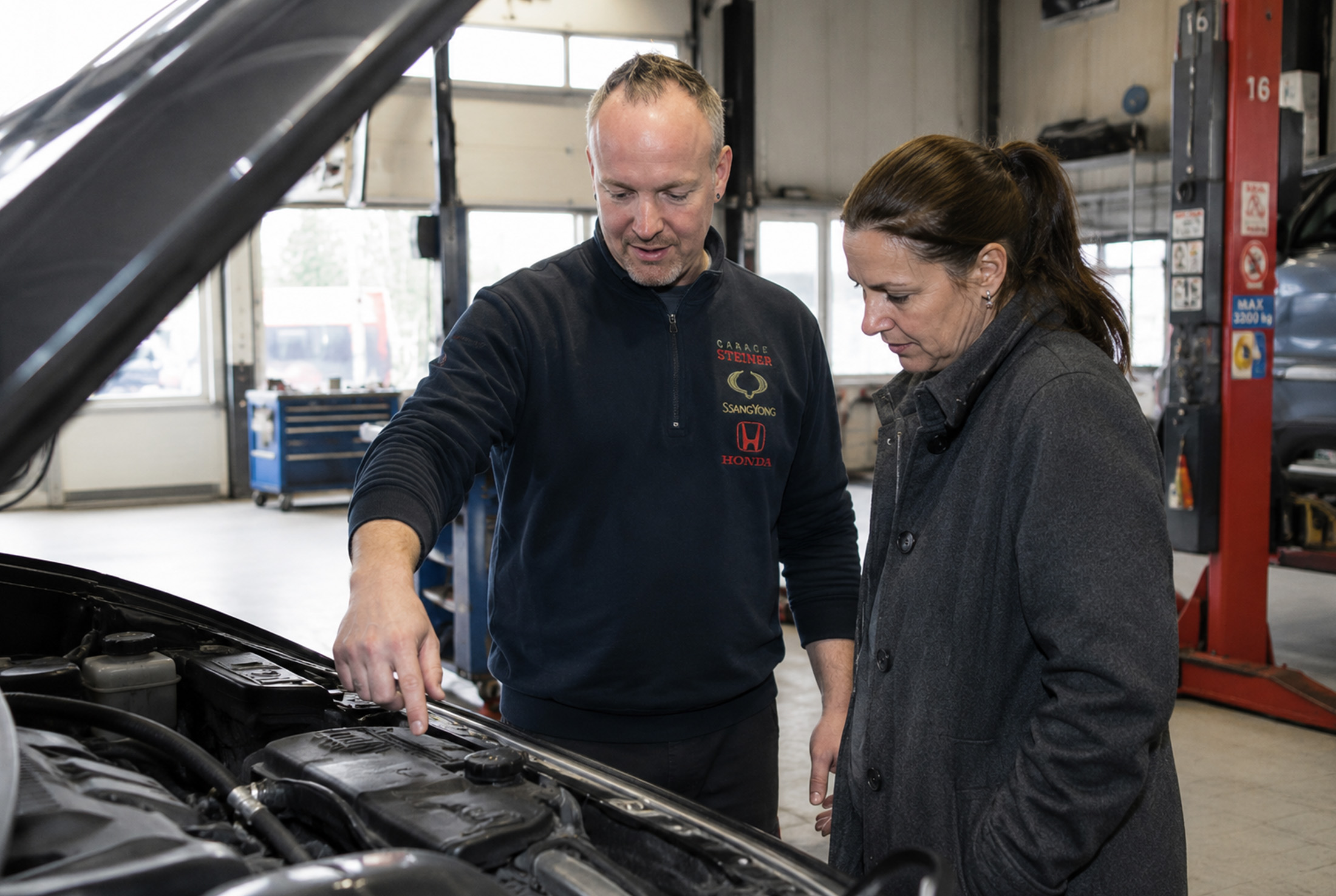 Mechaniker im Gespräch mit einer Kundin neben dem offenen Fahrzeug